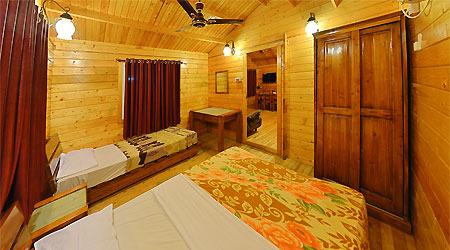 Woodencottage with beds, fan, study table and dining table in the adjoining room in Bluebay beach resort