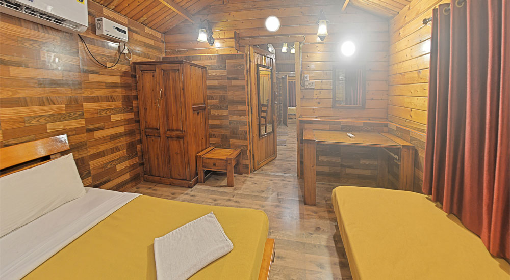 Woodencottage with beds, fan, study table and dining table in the adjoining room in Bluebay beach resort